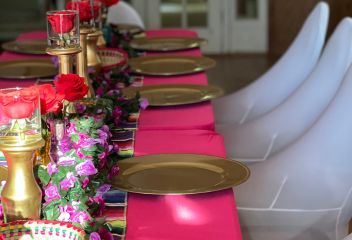 Dining table set up with a pink table cloth, gold plates, and floral decorations